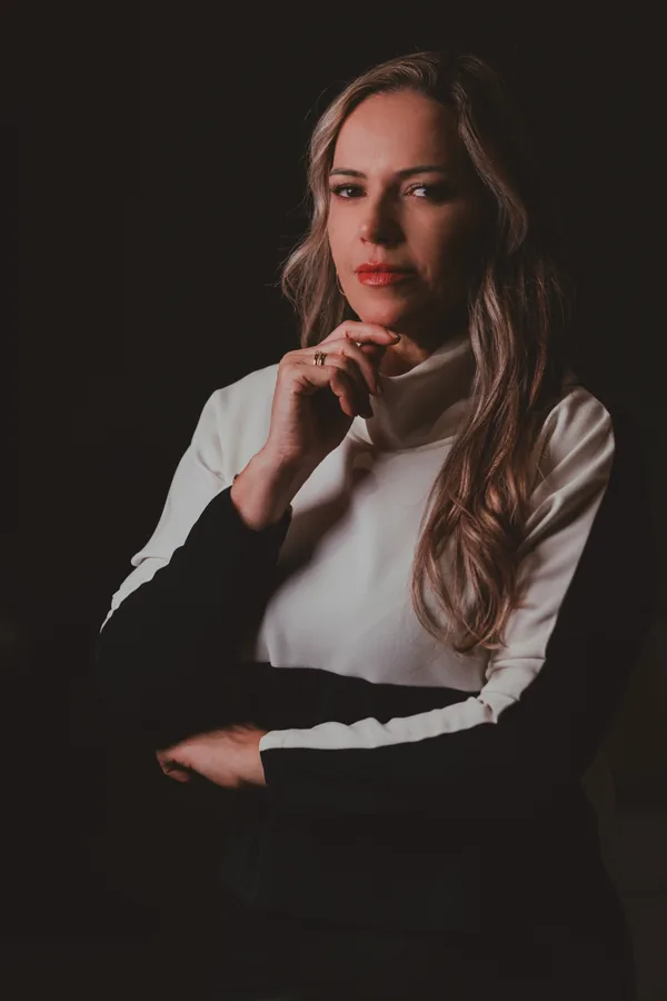 Retrato da Dra. Vanessa Benetti Di Sessa em estúdio, com blusa de gola alta e mão no queixo