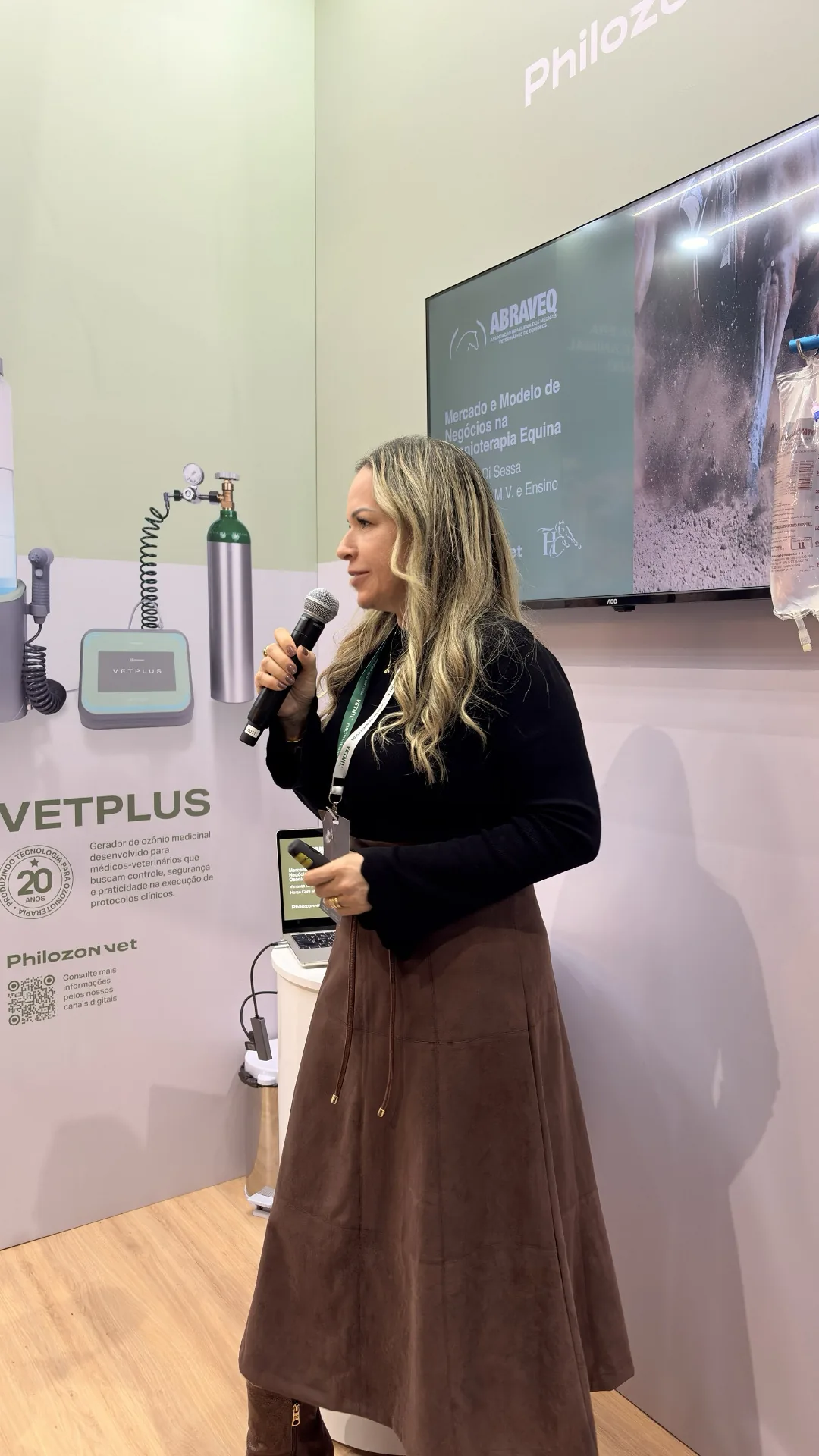Dra. Vanessa Benetti Di Sessa, de microfone, palestra sobre ozonioterapia equina em estande de congresso veterinário