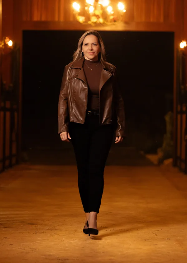 Dra. Vanessa Benetti Di Sessa caminhando pelo corredor de uma cocheira iluminada por lustres